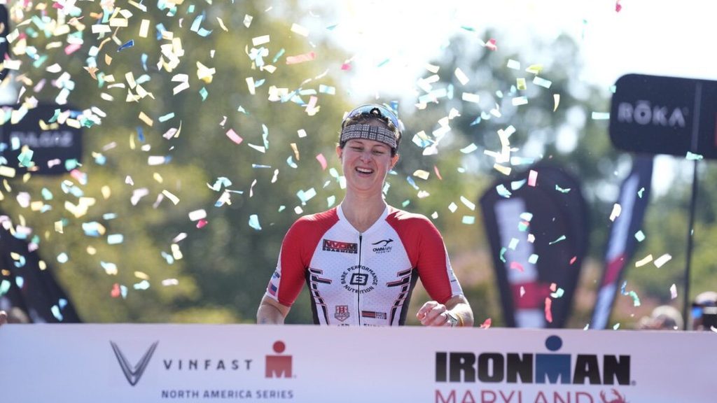 Элис Альбертс пересекает финишную черту Ironman Maryland 2023 под праздничным конфетти.