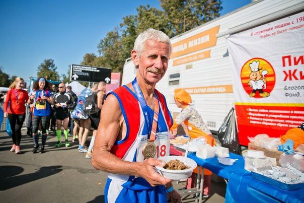 Спортсмен с финишной медалью держит тарелку еды у пункта питания после соревнования.